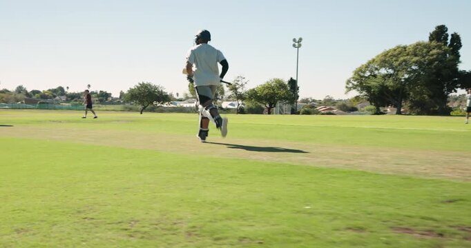 Cricket bat and helmet are resting on trimmed green pitch, featuring light pole, houses