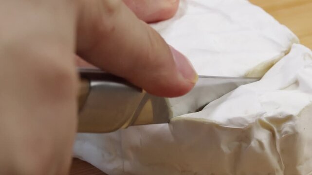 gros plan sur une main coupant un fromage ovale fondant 