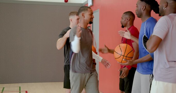 Hugging diverse male friends greeting inside gym lobby with door handle, fire alarm bell