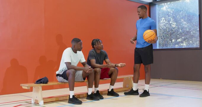 Entering teammate with basketball urging african american teammates raising hand to play on gym