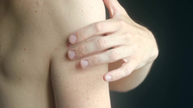 Close up of man touching pimple on his back and shoulder area, inspecting skin blemish with fingers. Skin problem, acne or irritation on shoulder blade. Man touching pimple on back shoulder close up