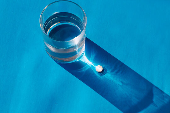 One medicine tablet pill in a sun caustic light flare near a glass of clean water.