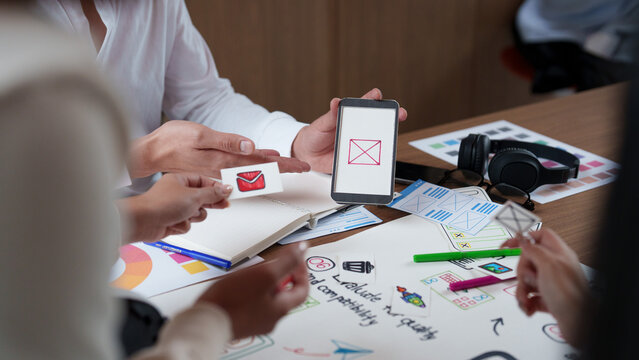 Creative design team prototyping mobile app interface with smartphone and paper mockups