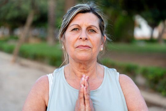 Senior woman practicing mindfulness and meditation in a park, joining hands in a prayer or namaste gesture