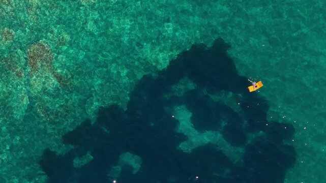 Aerial view of a person on a yellow inflatable mattress in the turquoise waters of Aquarium Beach in Jala, Vlore County, Albania.