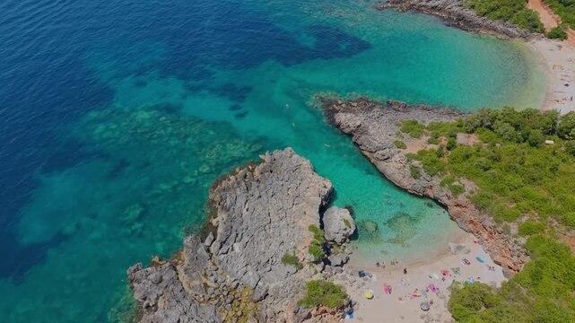 Aerial view of Aquarium Beach featuring crystal clear turquoise water, rugged rocky cliffs, and lush green vegetation on the coast in Jala, Vlore County, Albania.