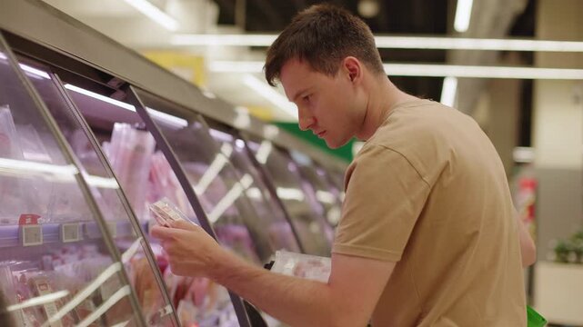 Young man choosing packaged meat products in supermarket refrigerated display