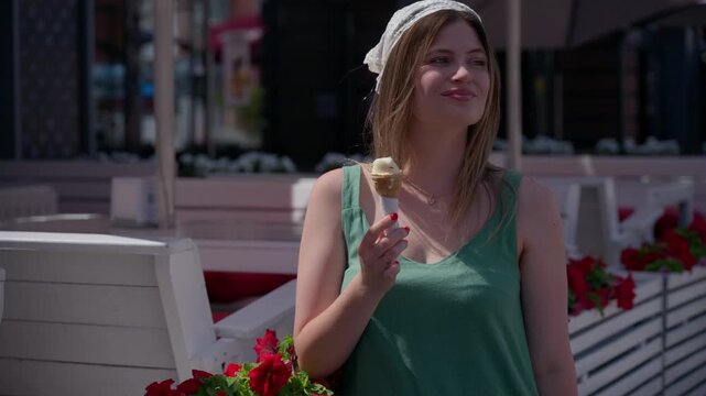 Young woman enjoys ice cream outdoors. She smiles, shields her eyes from sun. Summer day, relaxed, joyful mood. Perfect for vacation, leisure, or summer lifestyle scenes