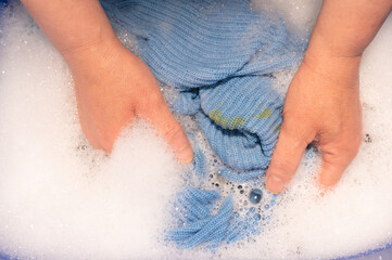 Fototapeta premium Washing dirty clothes with stains, hand wash, bowl with detergent, dirt spot or smudge on blue wool sweater, spill food or drink on shirt