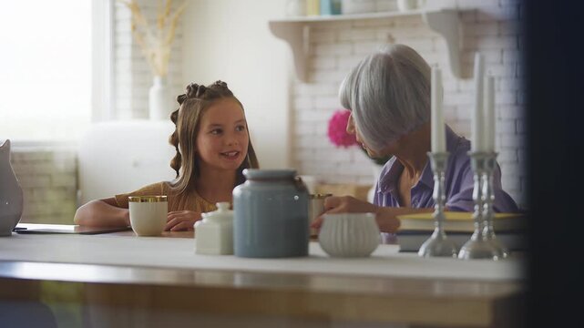 Happy granddaughter and her grandma talking and drinking tea, family pastime