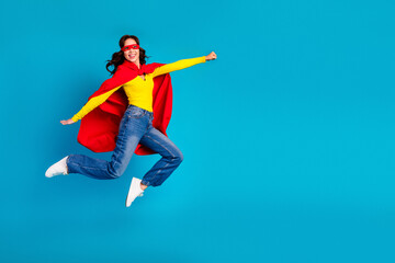 Fototapeta premium Young chic woman jumps in bright red cape and yellow shirt against blue background