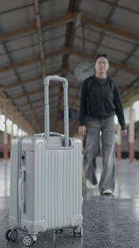 Rolling suitcase at a train station with traveler walking in background, ideal for travel, tourism, departure, arrival, public transport and journey concepts