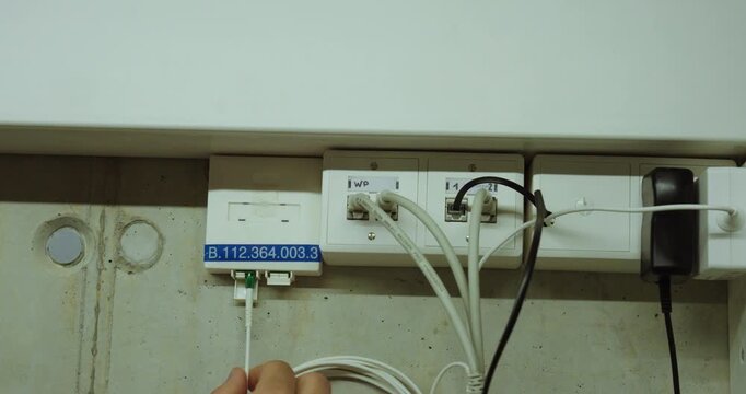 Person pointing at the identification number on a fiber optic wall outlet in a technical installation area.