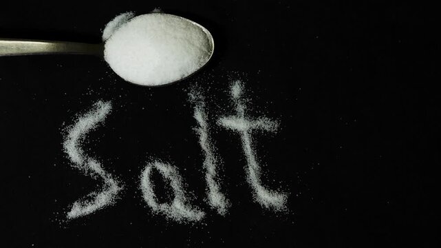 salt crystals arranged as text with spoon on dark backdrop highlighting cooking ingredient concept
