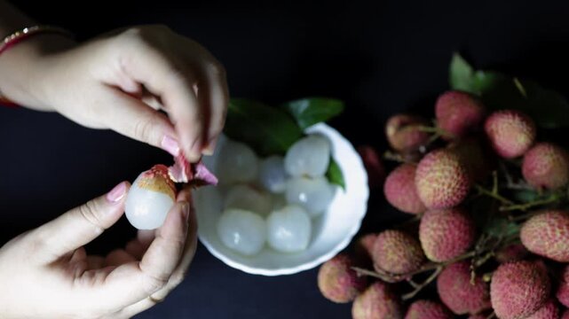 hands peeling off ripe lychee fruit from harvested bunch with green leaves