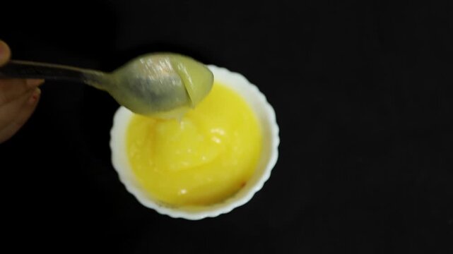 spoonful of homemade clarified butter with bowl of golden ghee on black background