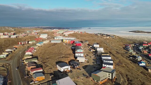 Wide drone tracking shot of a semi-circular residential housing development situated along a rocky hillside in Iqaluit, Nunavut.