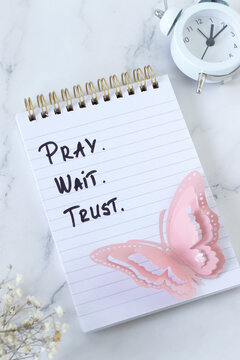 Pray, wait, trust, christian encouragement text in a notebook with alarm clock. Biblical concept of patience and faith in God Jesus Christ.