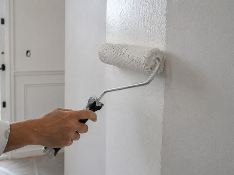 Application de peinture blanche au rouleau sur un mur int&eacute;rieur, travaux de r&eacute;novation et d&eacute;coration de la maison