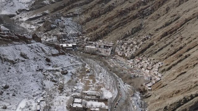 Hemis Monastery nestled in a snow-dusted valley in Ladakh, India, during winter. Aerial view captures a traditional Tibetan Buddhist architecture surrounded by barren mountain slopes and snowy ridges.