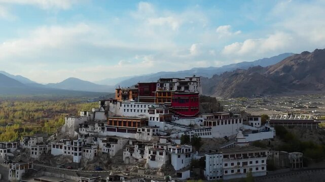 Thiksey Monastery sits atop a hill overlooking the Indus Valley with mountain ranges in the background. Slow lateral pan reveals the white and red Tibetan Buddhist architecture durng autumn season.