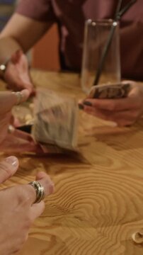 Vertical of hands of young woman counting US dollar bills at wooden table while splitting bill with friends at bar. Personal finance, budgeting, or casual dining commercials