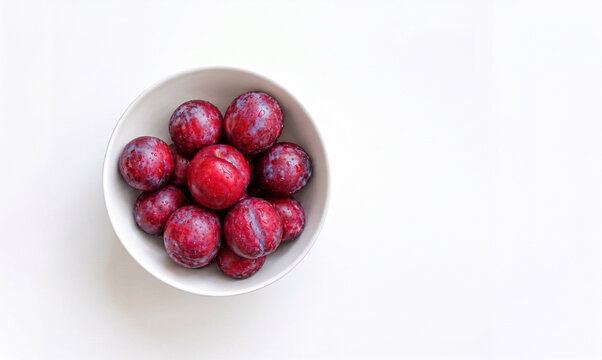 Fresh ripe plums in a white bowl on white background