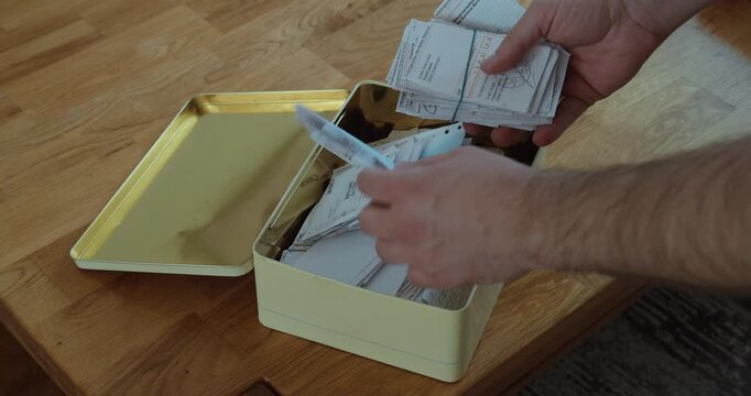 Person organizing and collecting old payment receipts and paper records in a storage box.