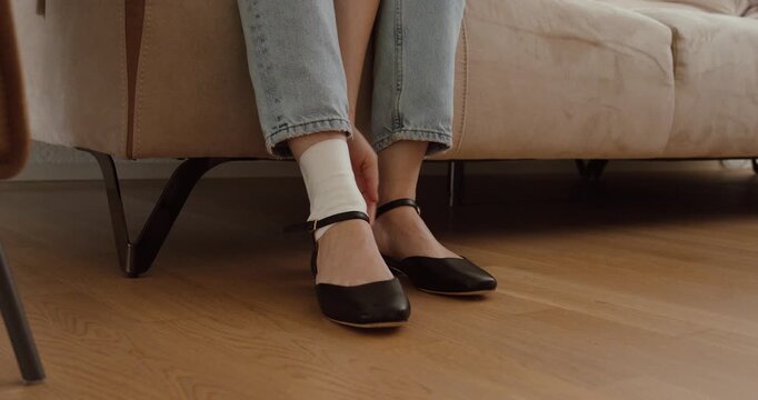 Woman sitting on a sofa with a bandaged ankle and visible foot discomfort. Suitable for healthcare, recovery, rehabilitation, pain management, and orthopedic concepts.
