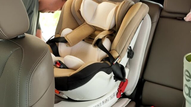A man adjusts a child car seat inside a vehicle. The setting is well-lit, highlighting the seat's design and safety features. Useful for parenting tutorials and safety guides.