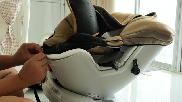 Close-up of hands tightening straps on a child's car seat in a bright, modern interior. Useful for parenting content or safety tutorials.