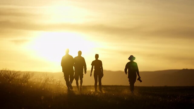Silhouettes of a group of friends walking together in nature at golden hour sunset, slow motion