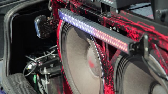 Custom car audio setup with multiple powerful subwoofers and red and black splatter design. LED light bar illuminates system, showcasing intricate wiring and installation for audio competition.