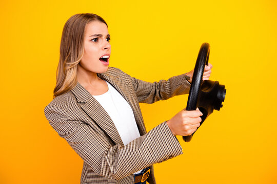 Surprised businesswoman gripping a steering wheel and reacting to sudden danger while pretending to drive against a bright yellow background
