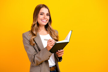 Fototapeta premium Smiling businesswoman writing in notebook against a bright yellow background, planning, taking notes and staying organized for work and personal projects