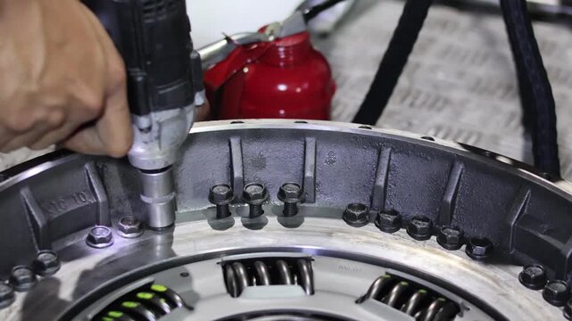 ​A close-up of a mechanic using an electric impact wrench to tighten bolts on an automatic transmission torque converter assembly.
