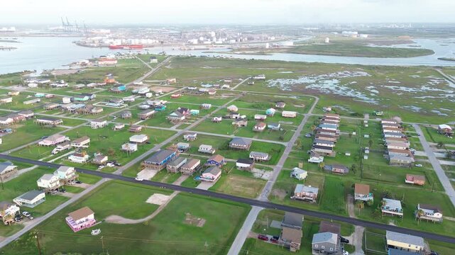 Seashell Dr neighborhood aligns toward Freeport Harbor Channel where cargo operations storage tanks frame northern horizon. Mixed roofing tones, bright sand patches define block in Freeport, TX