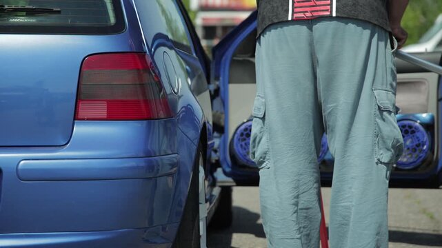 Rear view of blue car with open doors showcasing powerful audio system at an automotive competition, multiple speakers installed in door panels, enthusiasts gather for sound pressure level measurement