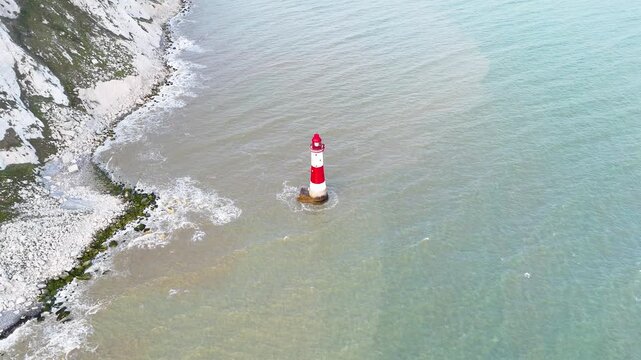 Drone aerial footage of a red and white lighthouse standing alone in coastal waters near dramatic chalk cliffs on the southern coast of England.