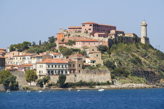 View of the historic buildings of the old town and the lighthouse on the rocky promontory overlooking the blue sea Portoferraio, Tuscany, Italy.