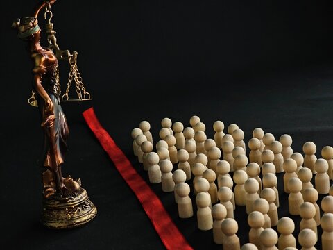 Justice stands before a crowd of wooden figures on a black background