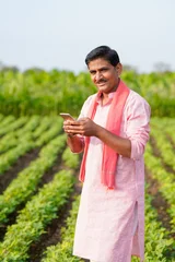 young indian farmer using smartphone standing at peanut field © PRASANNAPIX