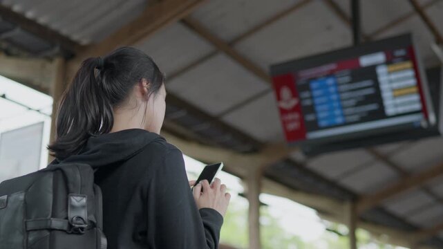 Traveler checking train schedule on a smartphone at railway station, ideal for travel planning, public transport, mobile ticket, departure and journey concepts.
