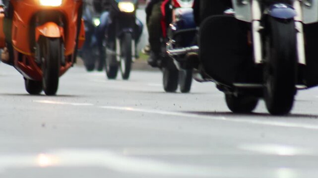 Low angle view of many motorcycles riding in formation on highway, chrome details and bright headlights visible on bikes, blurred background of riders and street during rally