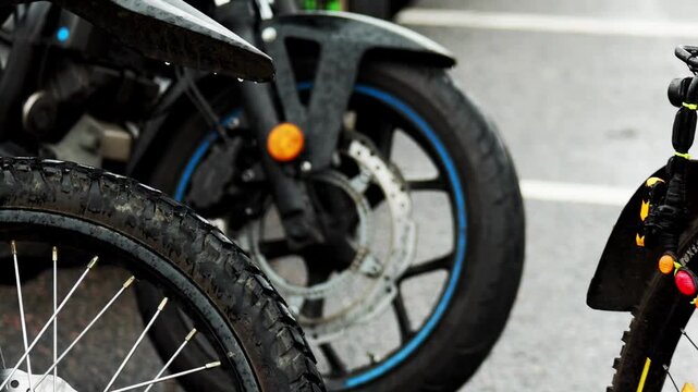 Detailed shot of two distinct motorcycle wheels side by side, foreground wheel featuring dirty knobby tire and spokes of dirt bike, background wheel showing smooth tire, alloy rim, and disc brake of r