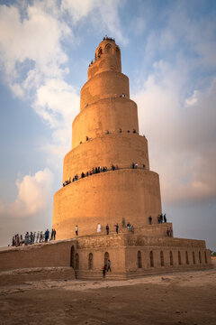 View of the historic Malwiya Tower with people climbing the external spiral ramp under a soft blue sky with clouds in Samarra, Saladin Governorate, Iraq.