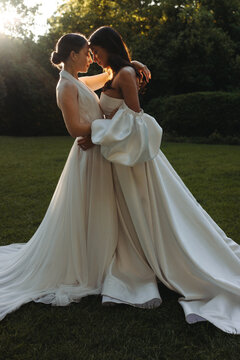Two brides embracing lovingly in a garden during sunset