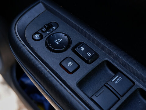 ​Car door control panel with power window switches, central door lock buttons, and side mirror adjustment controls, close up view of automotive interior components.