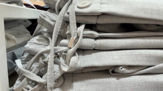 Stack of neatly folded gray aprons with metal clasps on wooden surface