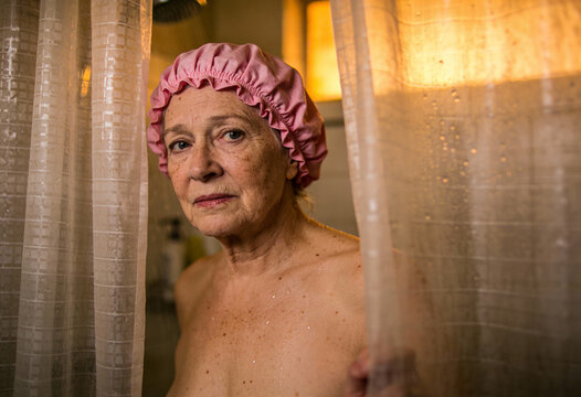 Seniorin um die 70 mit Duschhaube schaut hinter dem Duschvorhang hervor &ndash; K&ouml;rperpflege und Altern im Alltag